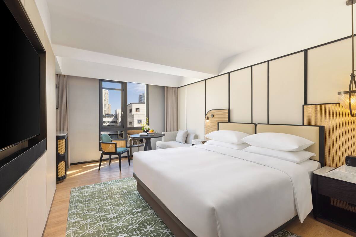 A modern hotel room with a large bed, a desk, and a television.