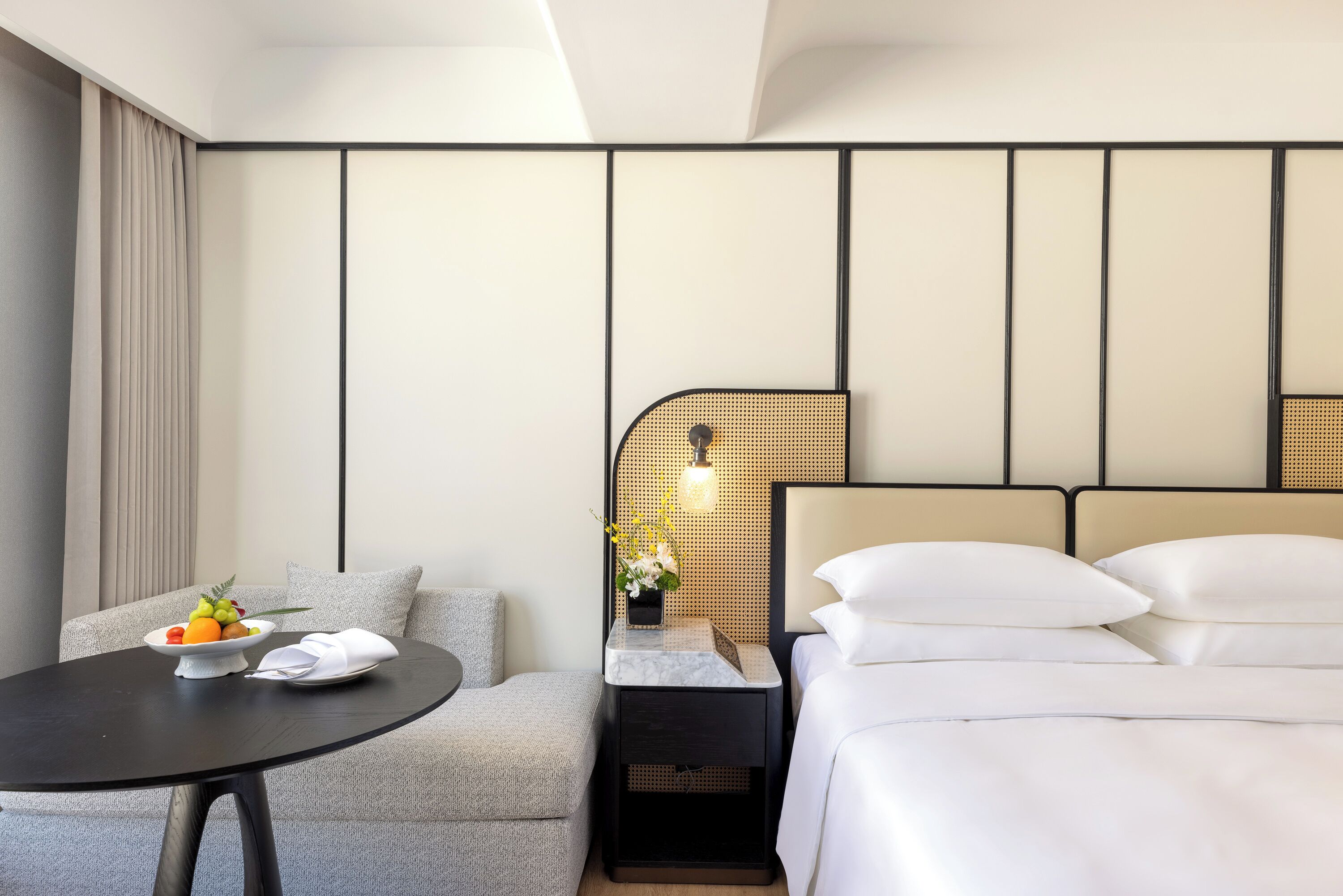 Une chambre d’hôtel avec un lit, une petite table sur laquelle se trouve un panier de fruits, une table de chevet avec une lampe et un canapé.