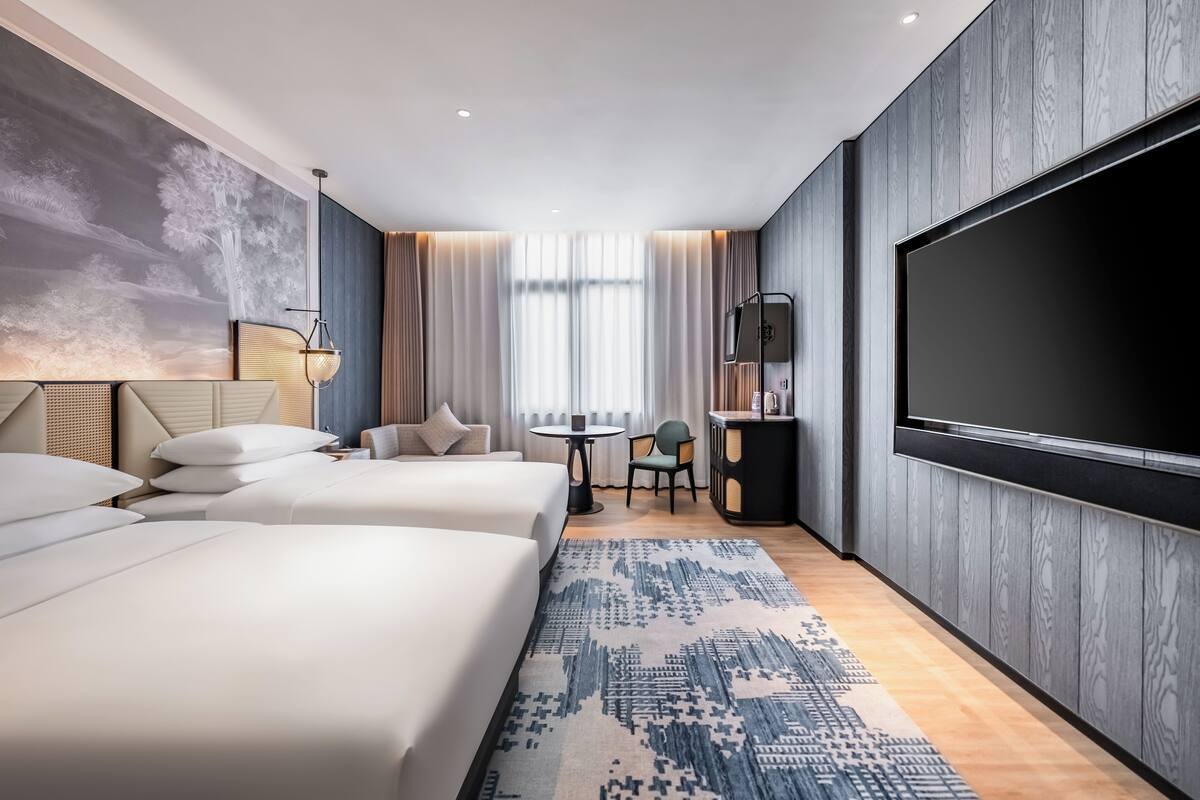 A hotel room with two beds, a large TV, a small table, and a chair.