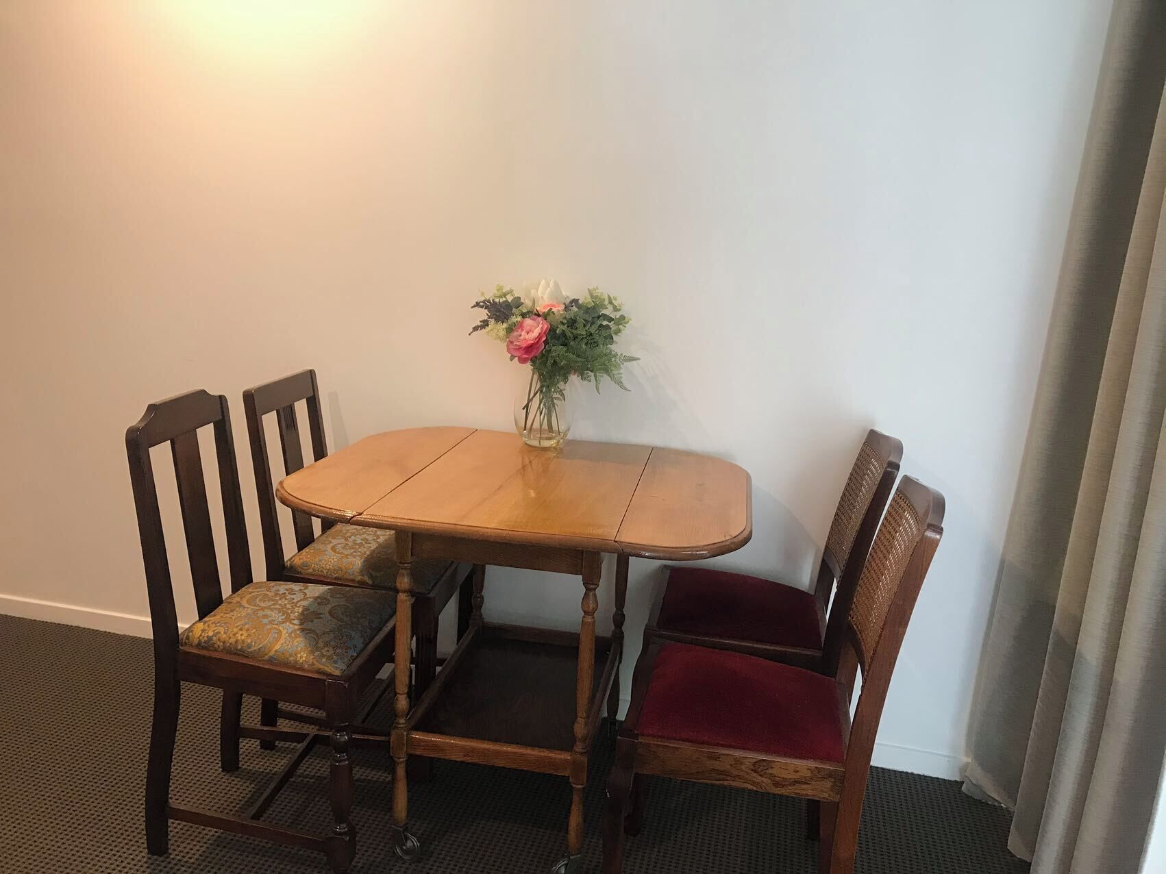Een klein eetgedeelte met een houten tafel en vier stoelen, waarvan er één een rode kussen heeft.