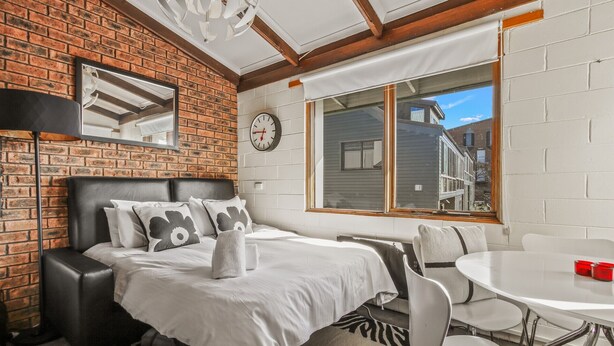 A modern room with a brick wall, a large window, a bed with a headboard, a small table, and a chair. - Alpine Haven 6 - Mt Hotham (Hotham Heights)