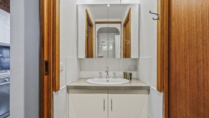 A bathroom with a white sink, two faucets, a mirror, and wooden doors. - Alpine Haven 6 - Mt Hotham (Hotham Heights)