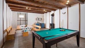 A pool table with a green felt surface, a wooden bench, a dining table with chairs, a kitchen area with blue cabinets, and a fireplace. - Casa Sole Istria by Villas Guide (Labin)