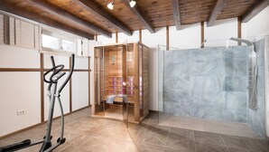 Een moderne badkamer met een douche, een houten sauna en een fitnessapparaat.