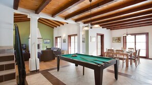 Um quarto espaçoso com mesa de bilhar, área de refeições e escada para outro andar.