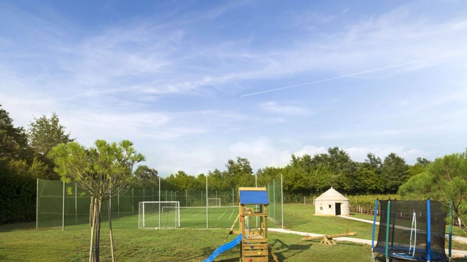 Ein eingezäunter Außenbereich mit Spielplatz, einem kleinen Gebäude und einem Fußballtor.