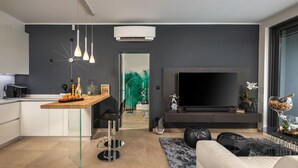 Una sala de estar moderna con televisor, sofá y zona de cocina con barra.