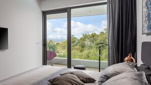 Un dormitorio con cama, televisor y balcón con vistas a árboles y un cielo nublado.