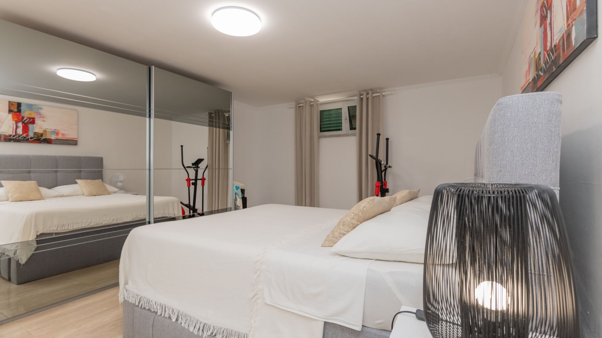 Ein modernes Hotelzimmer mit einem großen Bett, einem Spiegel, Fitnessgeräten und einem Ventilator.