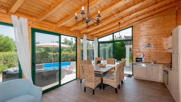 A wooden cabin with a dining area, kitchen, and a glass door leading to a pool. - Villa Lara by Villas Guide (Kamenmost)