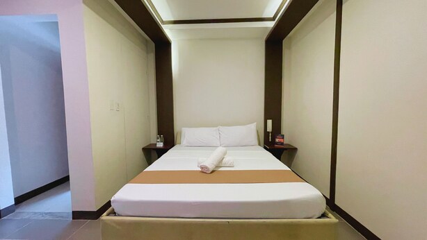Une chambre d’hôtel avec un lit, une table de chevet et un luminaire fixé au mur.