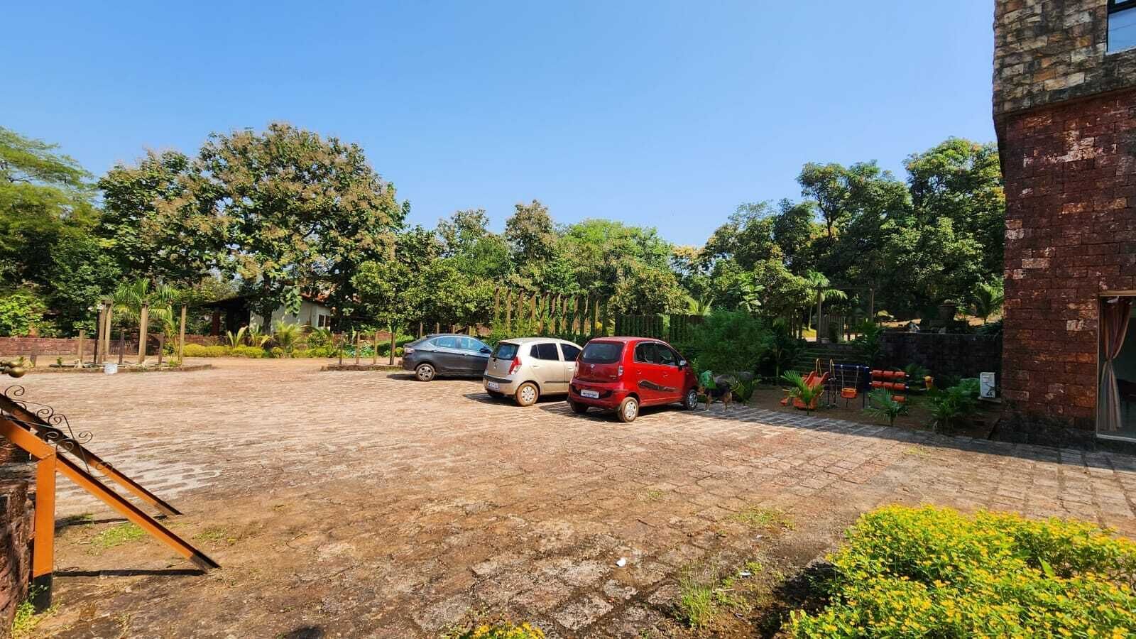 A parking area with three cars, a brick building, and surrounding greenery.