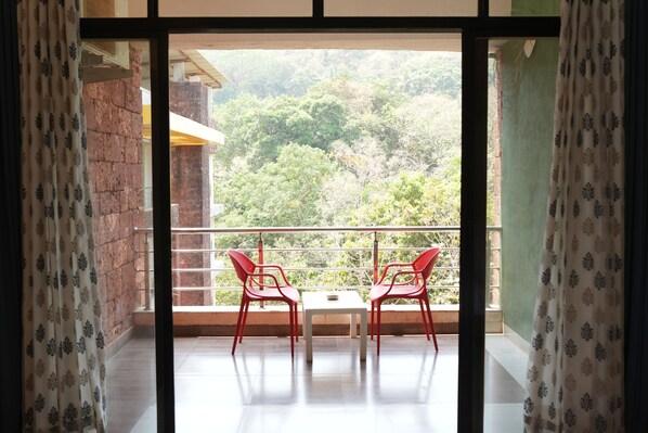 Un balcón con dos sillas rojas y una mesa, con vistas a una colina verde exuberante.