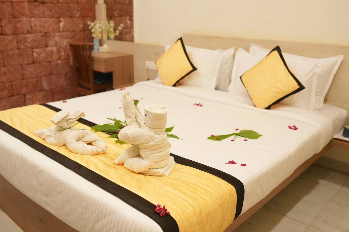 A neatly made bed with a white and yellow bedspread, two pillows, and a towel arrangement on the side.