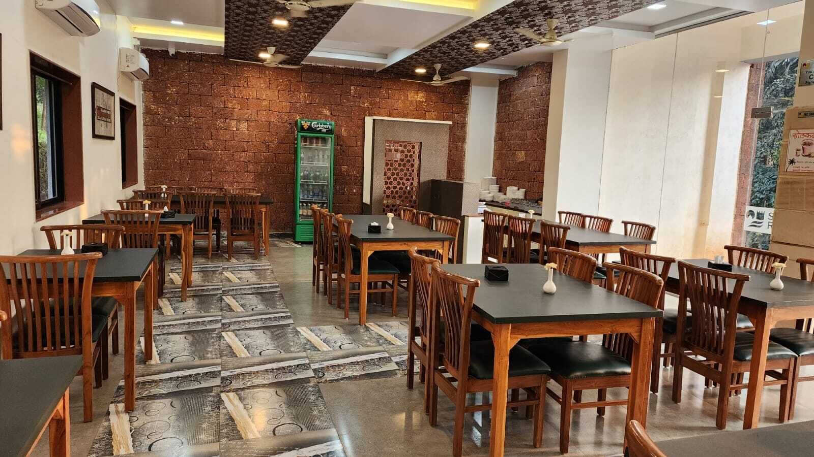 A restaurant with wooden tables and chairs, a brick wall, and a green vending machine.