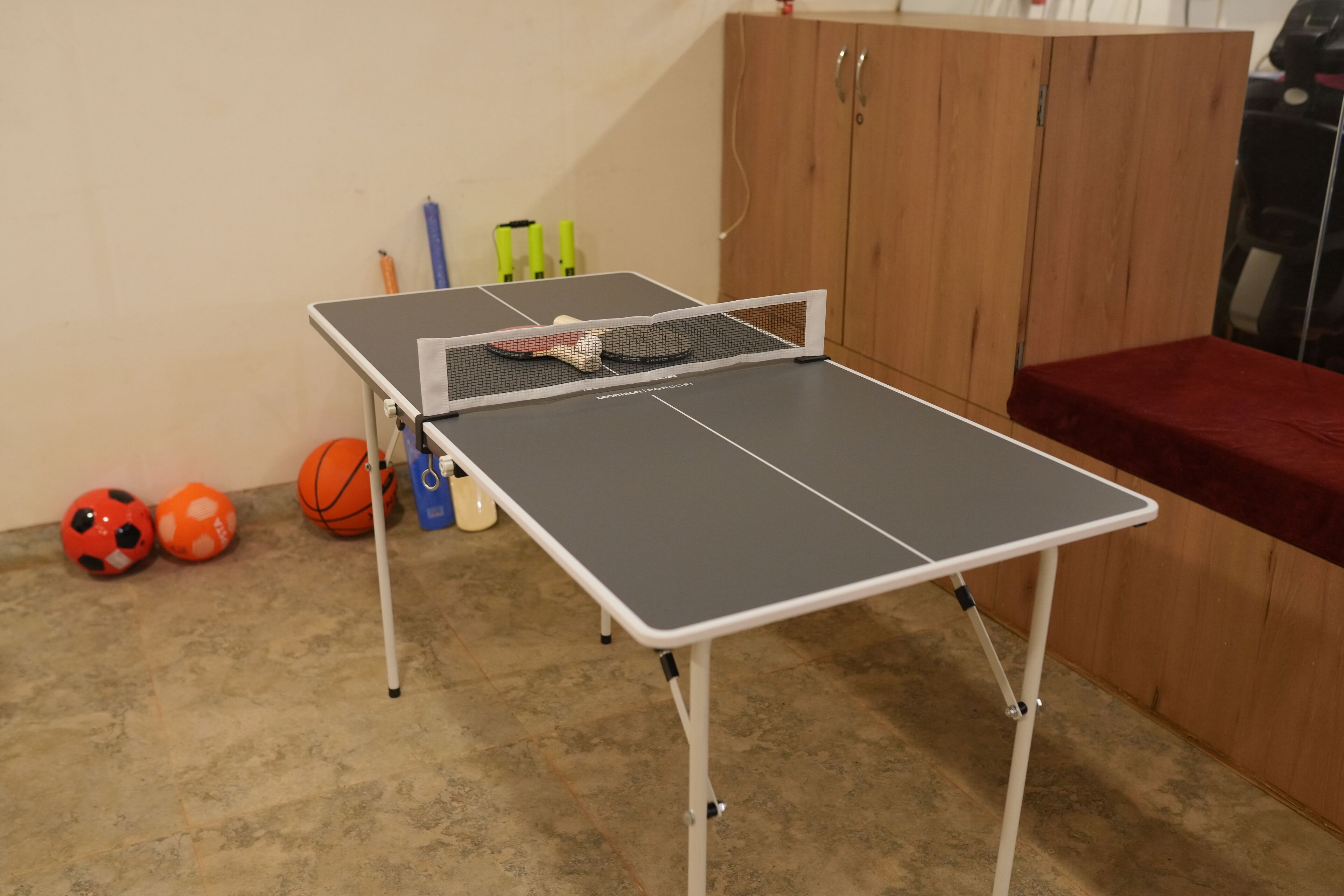 Een tafeltennistafel in een kamer met een houten kast en een rode bank.