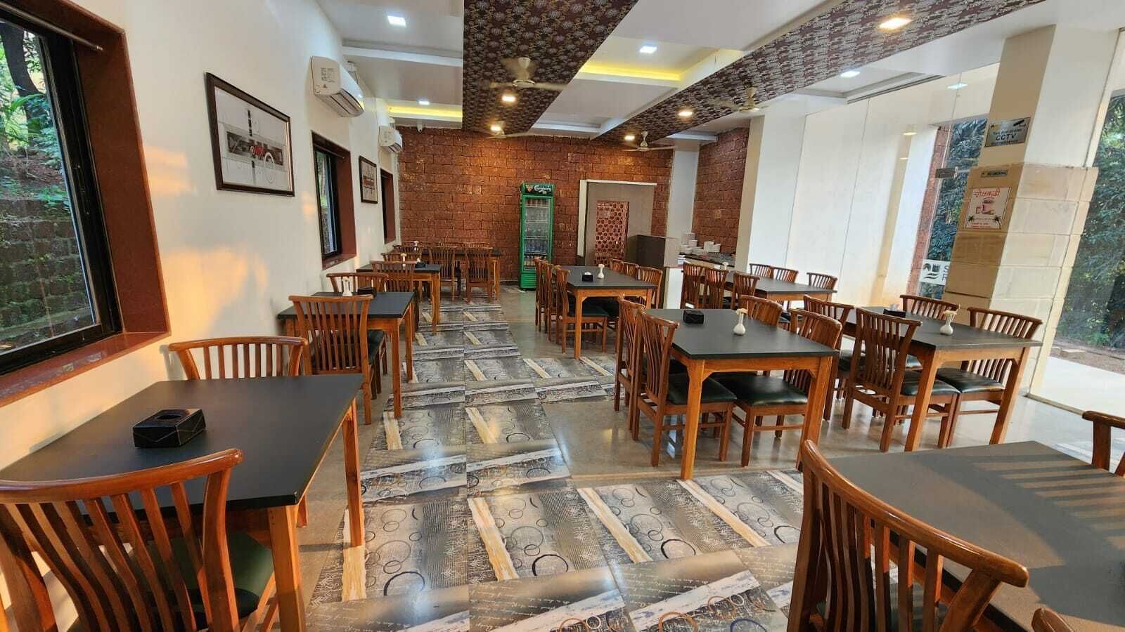 Un restaurant doté de nombreuses tables et chaises en bois, d’un sol à motifs, de murs en briques et d’un ventilateur de plafond.
