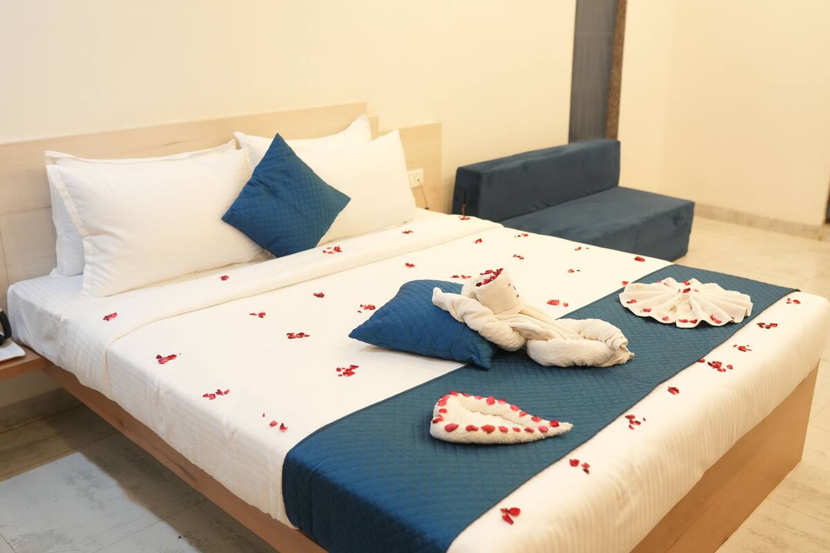 A neatly made bed with a blue and white bedspread, a plush teddy bear, and heart-shaped towels.