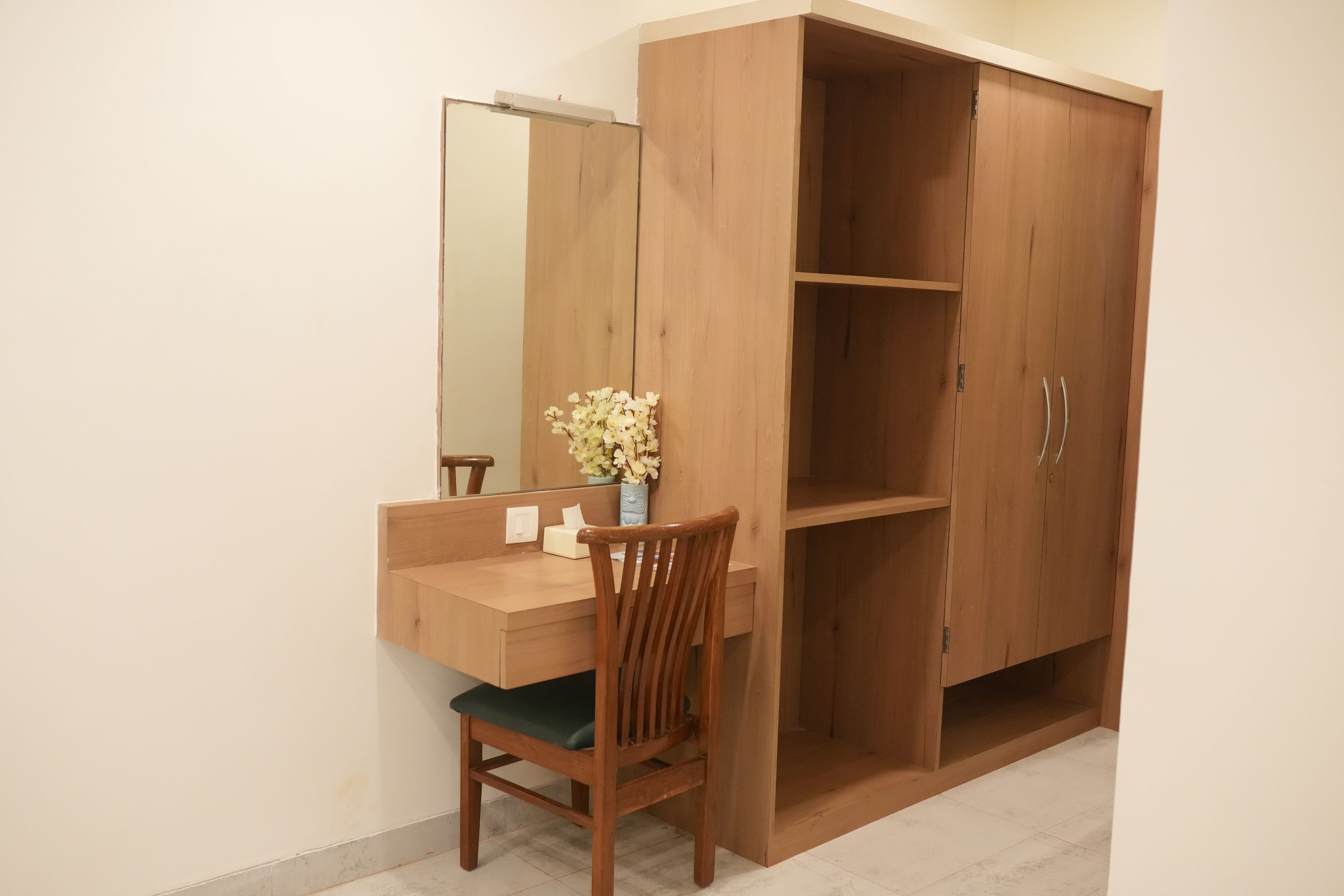 A wooden desk with a chair, a mirror, and a vase with flowers.