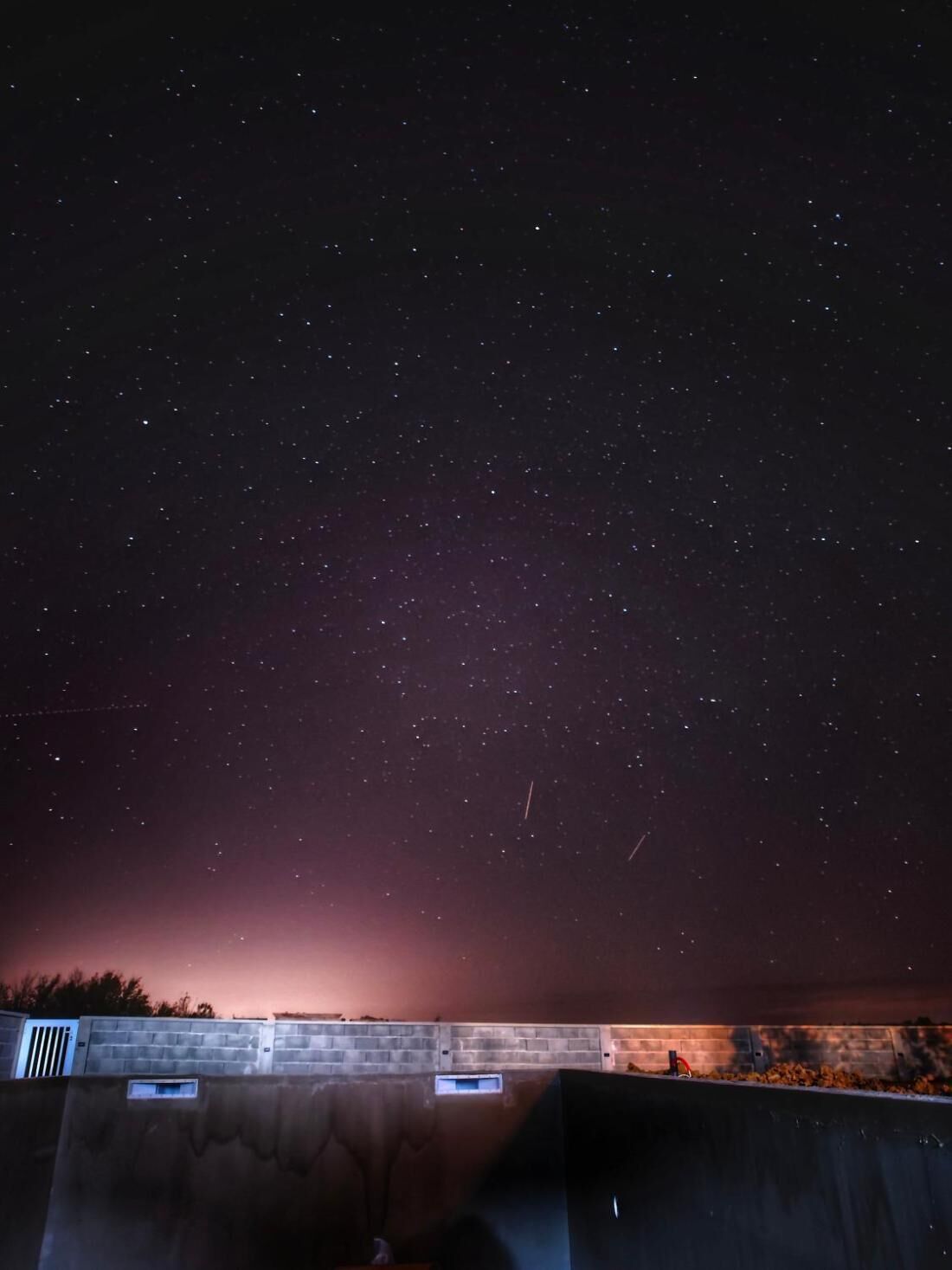 A night sky filled with stars above a brick wall with a small window.