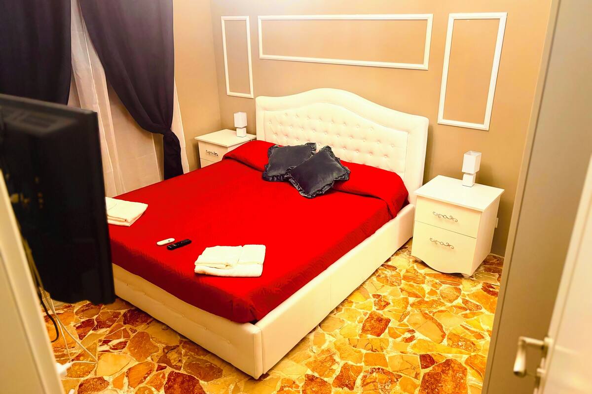 Ein Hotelzimmer mit roter Bettdecke, weißem Kopfteil und einem Boden mit Steinmuster.
