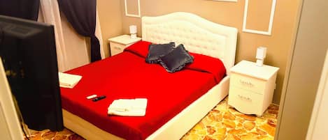 Ein Hotelzimmer mit roter Bettdecke, weißem Kopfteil und einem Boden mit Steinmuster.