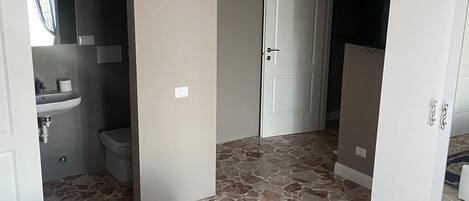 Una habitación con una colcha roja, un candelabro, un baño con lavamanos e inodoro, y un armario.