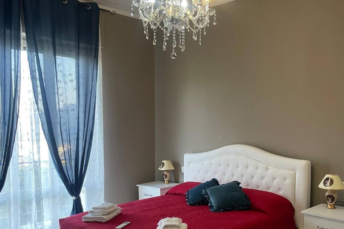 Ein Schlafzimmer mit einem weißen Bett, roter Bettwäsche, einer Chandelieber und einem gemusterten Teppich.