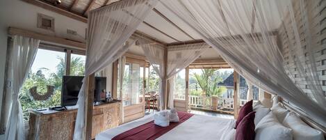 A bedroom with a canopy bed, a TV on a wooden cabinet, and a balcony with a view of palm trees.