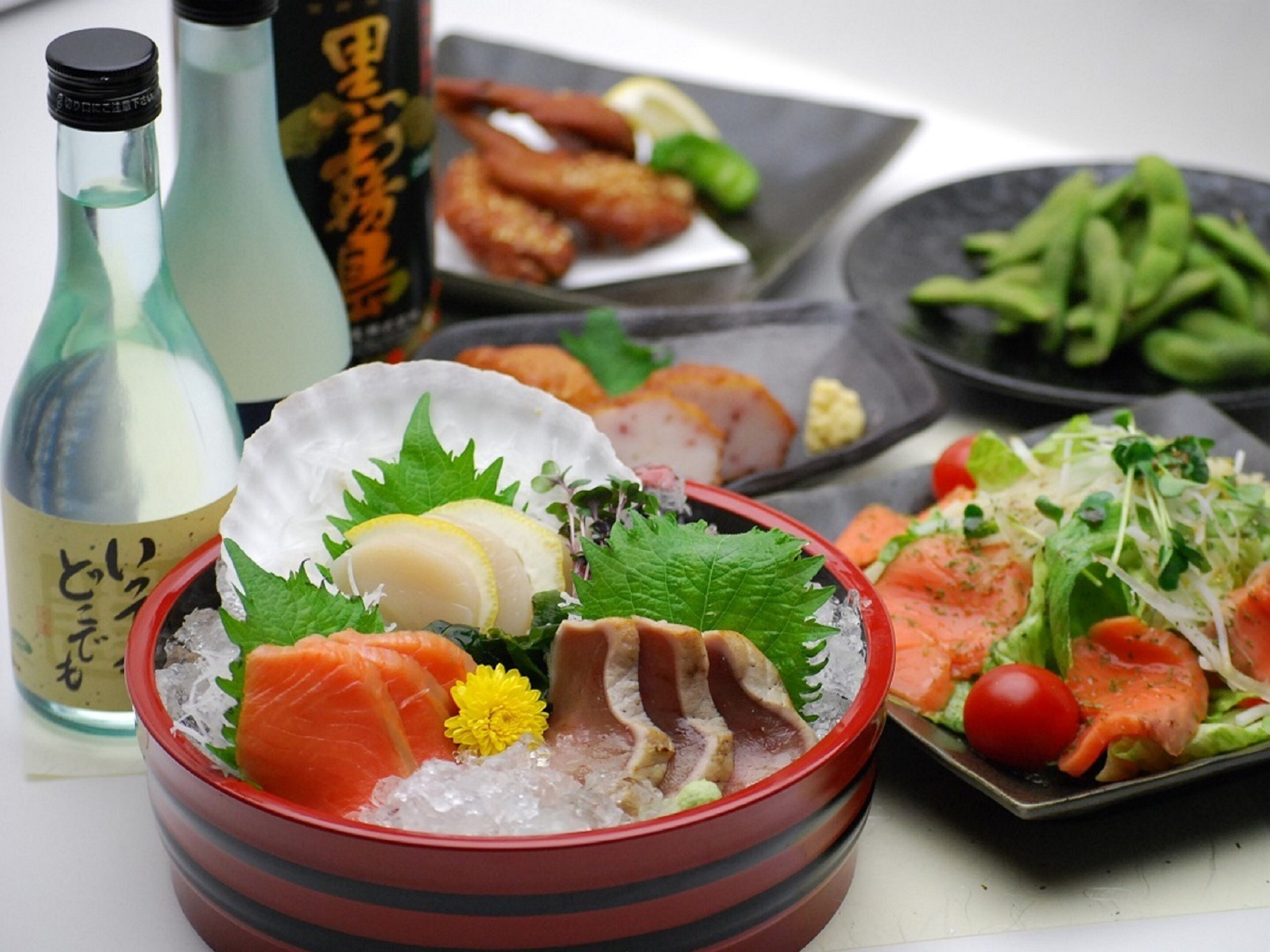 Forskellige japanske retter, heriblandt sashimi, en skål is med skaldyr og en tallerken med grøntsager.