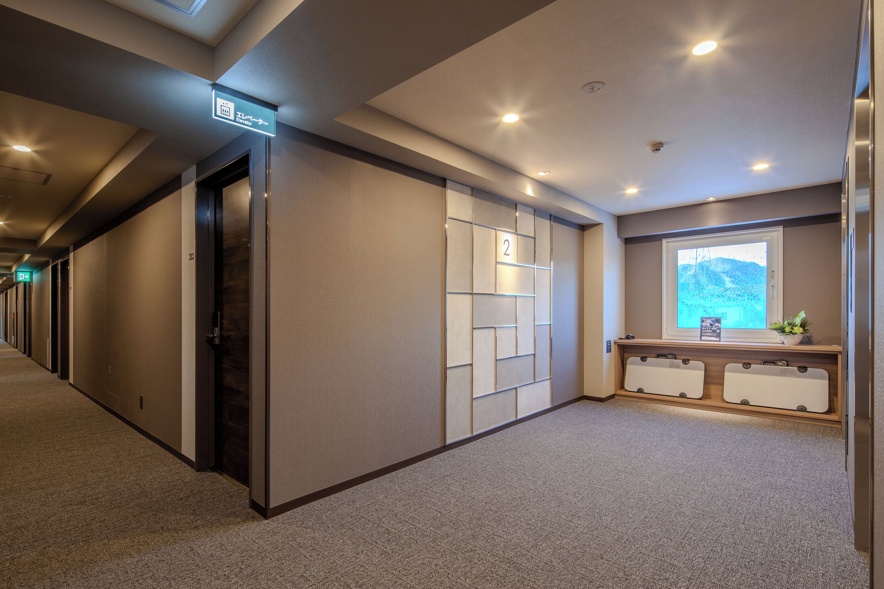 Un couloir d’hôtel avec un espace de réception, une fenêtre donnant sur un paysage agréable et une porte portant le numéro 2.