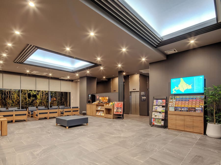 A modern lobby with seating, a reception desk, a digital screen, and a plant.