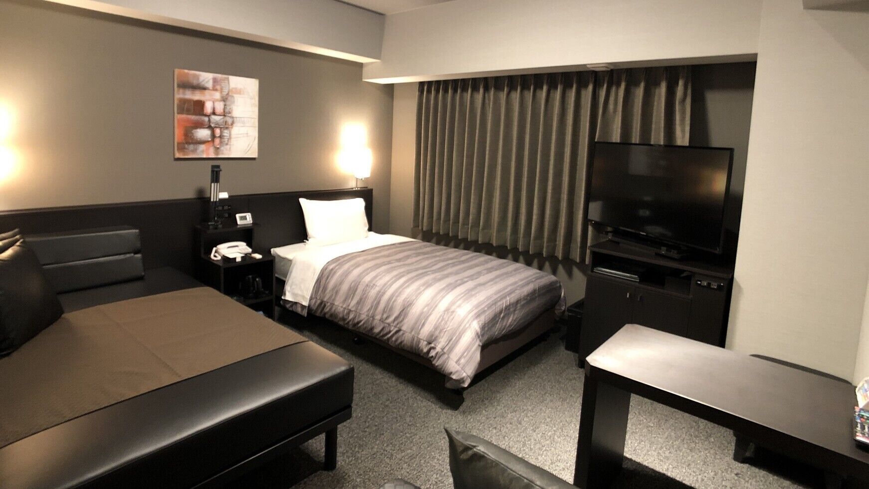 A hotel room with a bed, a desk, a chair, a TV, and a nightstand.