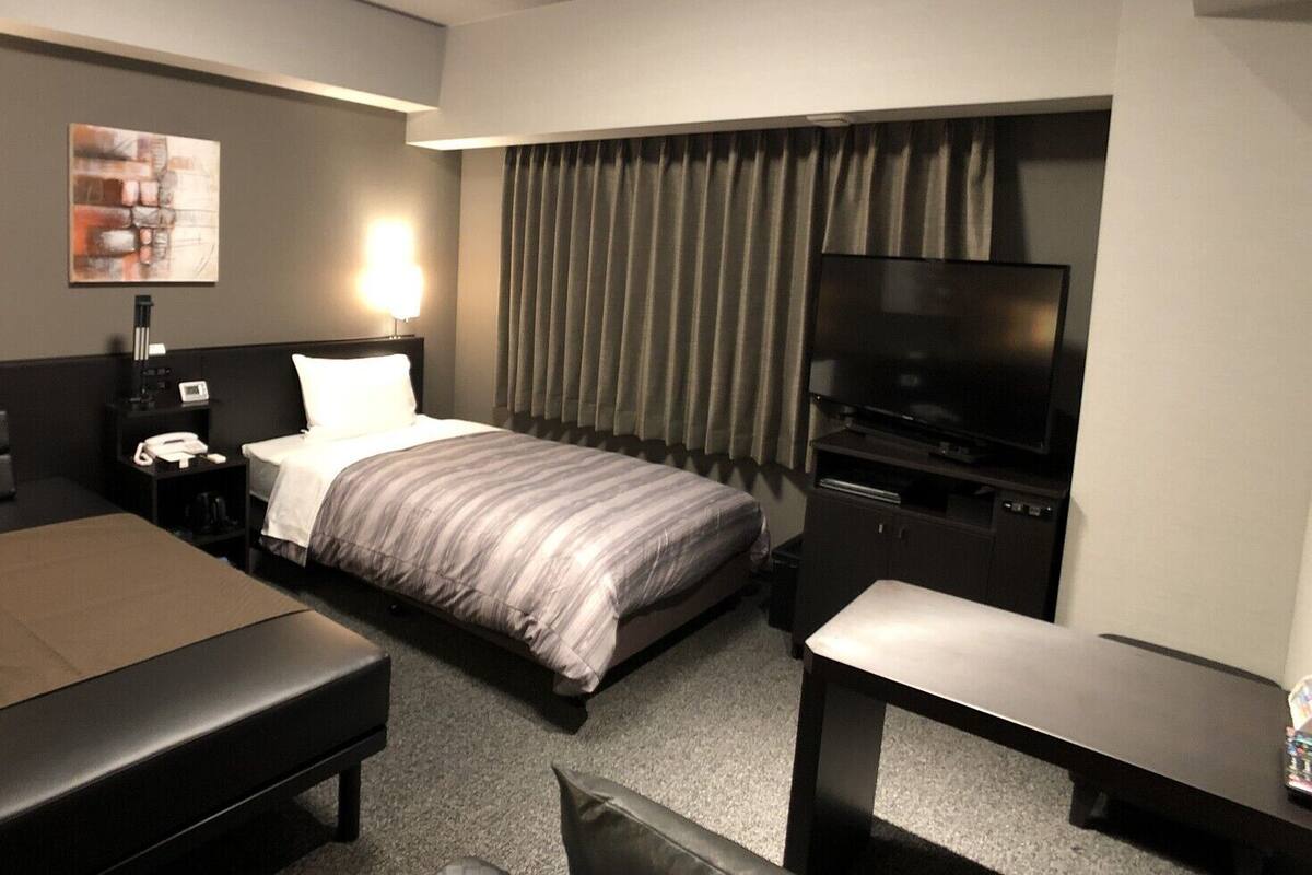 A hotel room with a bed, a desk, a chair, a TV, and a nightstand.