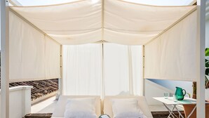 Un lit confortable installé à l’extérieur, doté d’un auvent, une petite table avec des verres et une carafe, et une vue sur la terrasse.