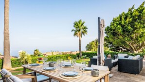 Une terrasse en bois avec une table dressée pour les repas, des sièges d’extérieur et une vue sur l’océan.