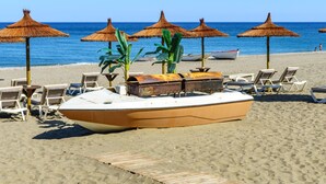 A beach with lounge chairs, thatched umbrellas, and a small boat. - Villa Sara by Interhome (Manilva)