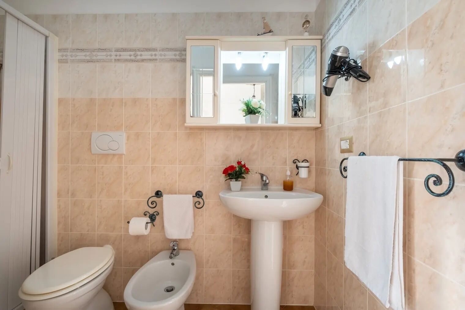 A bathroom with a toilet, bidet, sink, and a mirror above the sink.