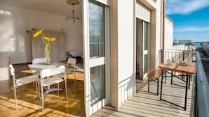 Un appartement moderne doté d’un balcon, d’un coin repas avec une table et des chaises, et d’une chambre avec un lit et un vase rempli de tournesols.