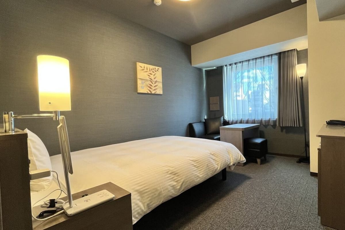Une chambre d’hôtel équipée d’un lit, d’un bureau, d’une chaise, d’une lampe, d’une télévision et d’une petite table.