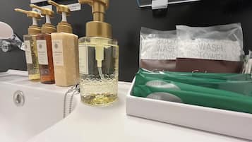 Un lavamanos de baño con diversos artículos de aseo, como champú, acondicionador y gel de ducha. También hay toallas verdes y una bolsa blanca con la etiqueta 'BODY WASH TOWEL'.
