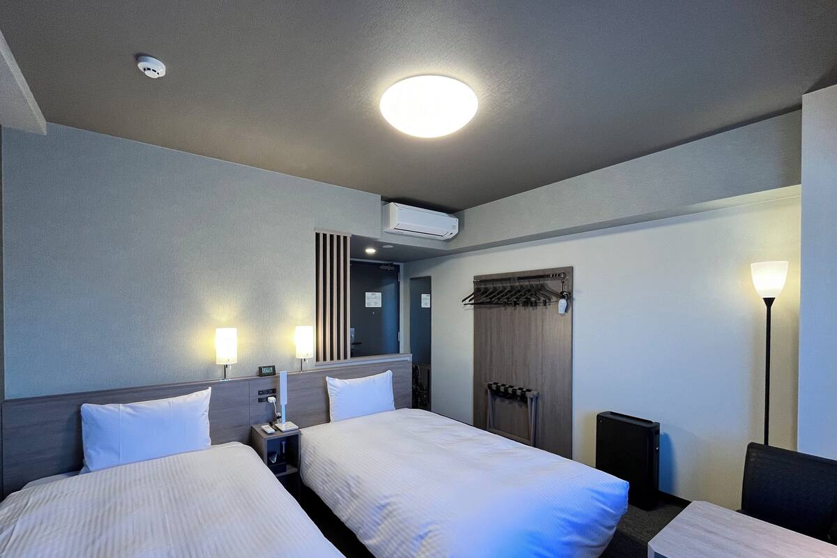 Une chambre d’hôtel avec deux lits, un bureau, une chaise, une lampe, une armoire et un miroir.