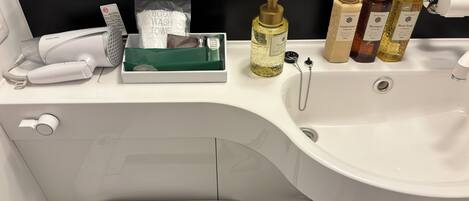 A modern bathroom with a white sink, a hairdryer, body wash, shampoo, and body soap on the counter.