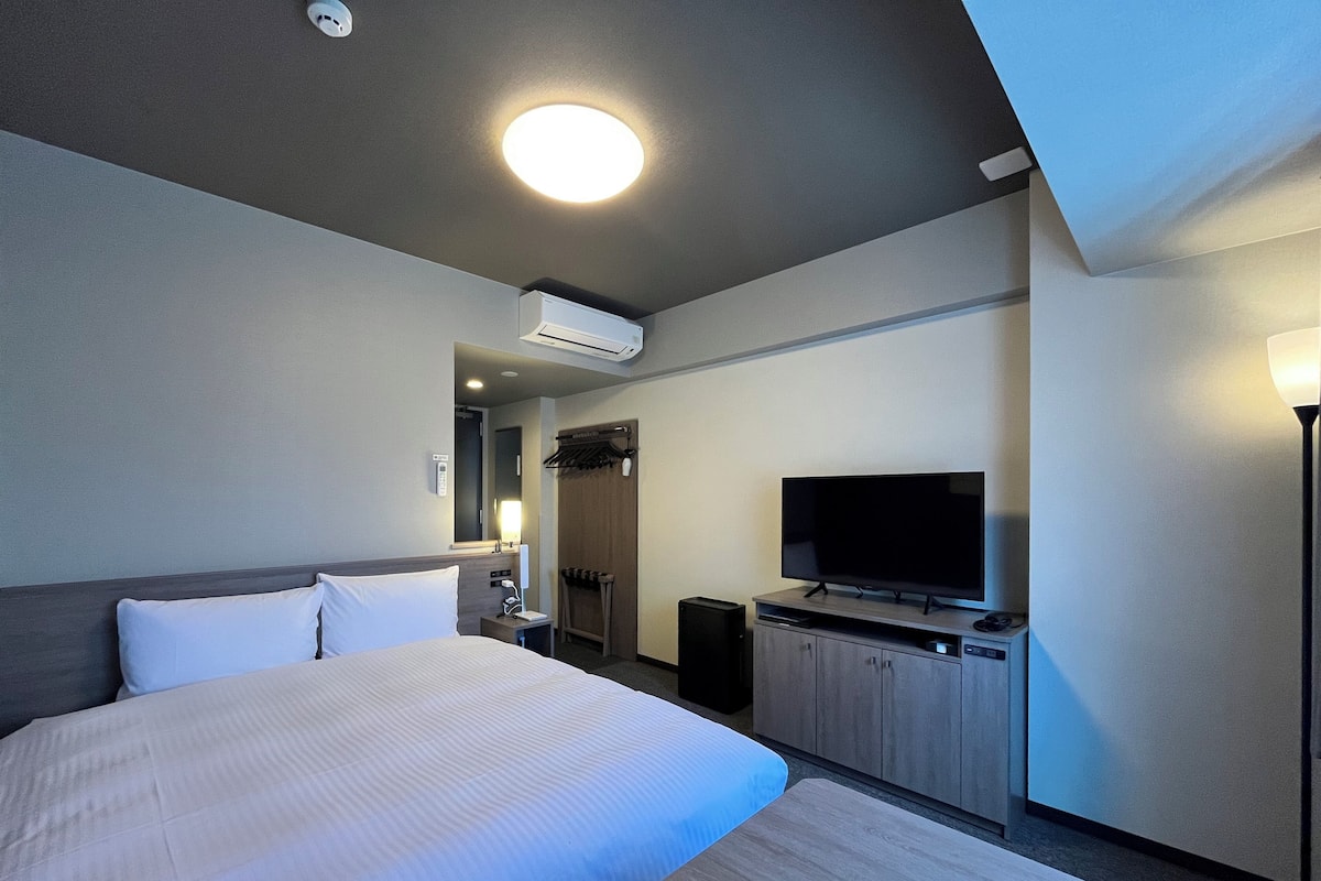 Une chambre d’hôtel dotée d’un grand lit, d’un téléviseur à écran plat, d’un bureau avec un ordinateur, d’une armoire et d’un appareil de climatisation.