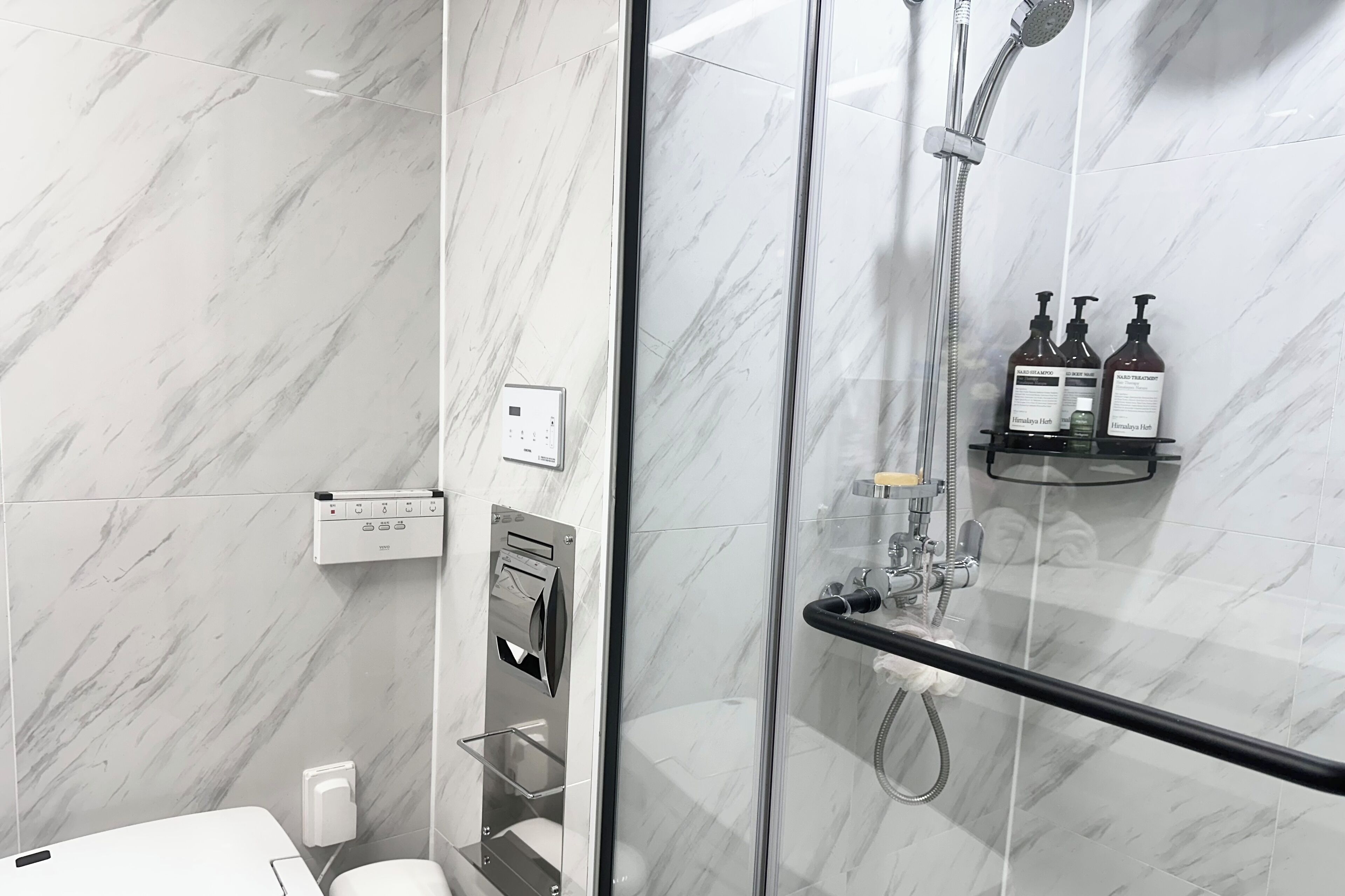 A modern bathroom with a glass-enclosed shower, marble walls, and a control panel.