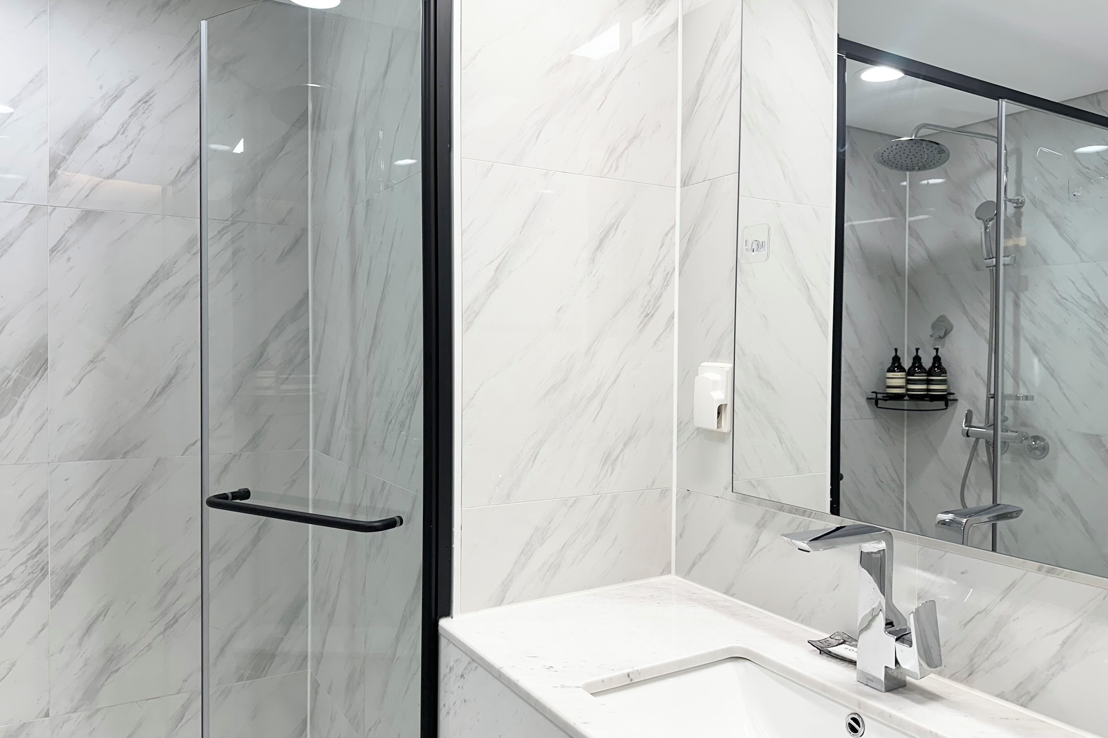 Une salle de bain moderne avec une douche à parois de verre, un comptoir en marbre blanc et un grand miroir.