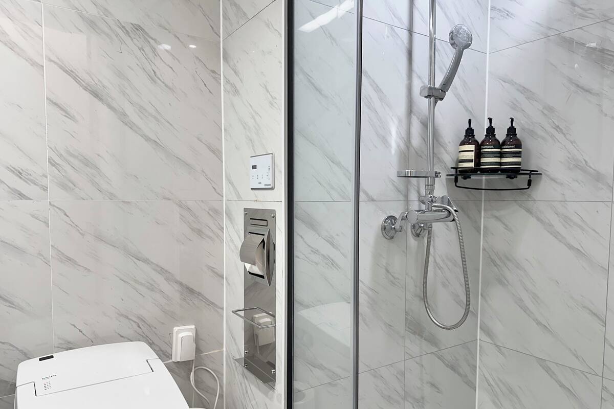 Une salle de bain moderne dotée d’une douche à parois de verre, d’une étagère intégrée pour le distributeur de savon et d’une prise électrique visible.