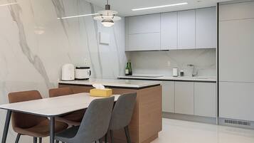 Una cocina moderna con armarios blancos, un protector contra salpicaduras de mármol y un comedor con mesa y sillas.