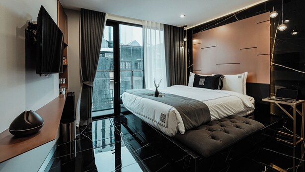 A modern hotel room with a large bed, a flat-screen TV, a desk, and a view of the city through large windows. - Hotel 433 - Asoke Sukhumvit (Bangkok)