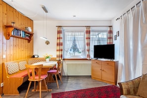 A cozy room with a wooden bench, a table, chairs, a TV, and a window with curtains. - Apartment 'Aretz' with Mountain View, Private Terrace and Wi-Fi (Feldberg (Schwarzwald))